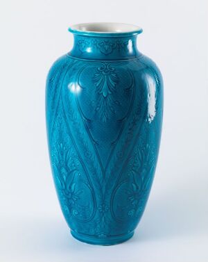  A vibrant turquoise vase with raised botanical patterns, reflecting light on its glossy surface against a plain light background. Artist name and title unknown.