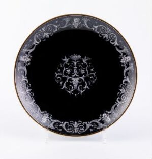  A decorative round plate with a glossy black surface and intricate light-colored scrollwork and a heraldic crest in the center, set against a white background. Artist and title unknown.