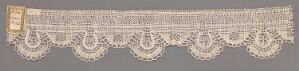  A photograph of a long strip of creamy beige vintage lace trim with a linear pattern featuring scalloped edges and teardrop floral motifs on a slightly darker beige background.