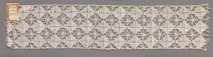  An elongated textile sample with a repeating diamond-shaped pattern in muted grays and beiges, featuring a stylized floral design within each diamond, and a distinct golden yellow strip at one end. Artist name and title are unknown.