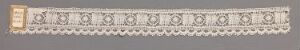  A narrow decorative strip with a repeating pattern featuring a left block with gold square and rectangular embellishments and a main section with interlinked circular and oval grayscale floral designs on a pale grey background.