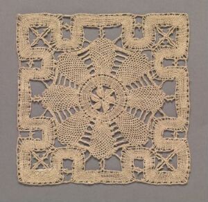 
 An antique, square-shaped piece of lace or openwork embroidery, featuring a symmetrical, star-like pattern with radiating points and intricate X-shaped crosses, set against a muted background.