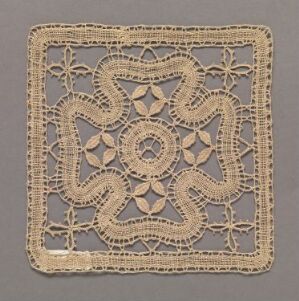  A square piece of intricate cream-colored lacework with a symmetric floral pattern is displayed against a medium grey background. Artist name and title are unknown.