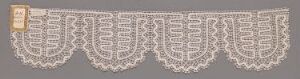  A strip of intricate creamy white lace with a repeating scalloped floral pattern set against a muted grey background. Artist name and title are unknown.