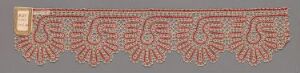  A decorative textile strip with a repeating pattern of red, coral, and turquoise motifs on a neutral background, possibly showcasing traditional embroidery, with a square label on the left end.