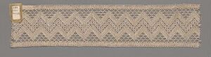  A vintage or antique narrow and long beige lace textile with a repetitive geometric zigzag pattern, presented against a neutral gray-brown background.