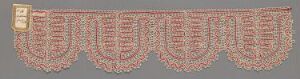  A horizontally elongated image of a textile piece with a muted beige background and intricate red and white scalloped patterns running along its length, featuring a distinct patch or emblem on the left side.