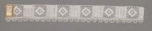  A long, narrow grey or off-white textile band with a repeating geometric pattern of diamond shapes and a checkerboard-like design at both ends, suggesting a traditional or folk art influence.