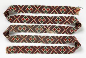  Three intricately patterned textile bands, featuring geometric designs in red, green, and black on a creamy white background, laid out parallel against a light grey surface.