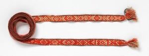 
 A reddish-brown decorative belt or sash with a pale orange geometric pattern laid out on a light background, featuring tassel-like fringes at both ends.