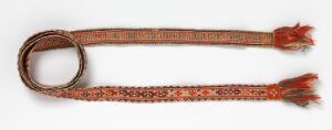  An intricately woven strap or belt with a loop on one end and red tasseled ends, featuring a pattern of geometric shapes in reddish-brown, tan, and orange on a plain light-colored background.