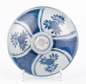  A round ceramic plate with a traditional blue and white floral pattern divided into quadrants, displayed on a clear stand.