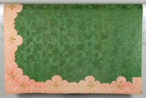  An ornamental rectangular textile or paper artifact with a central green area featuring subtle floral damask patterns, surrounded by a decorative border in a gradient from light peach to coral pink with stylized cherry blossom motifs.