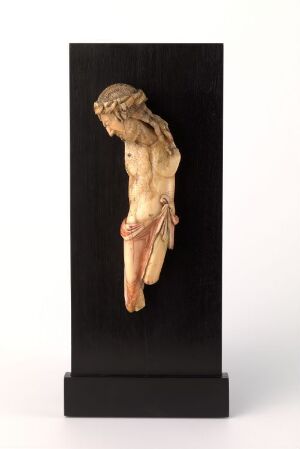  An intricately carved walrus ivory figure from a crucifix, titled "Del av krusifiks" by an unidentified artist, mounted on a black stand. The figure, potentially representing Jesus Christ, is depicted from the torso upwards with a bowed head and detailed hair, in a warm cream color with hints of beige, yellow, and light brown.