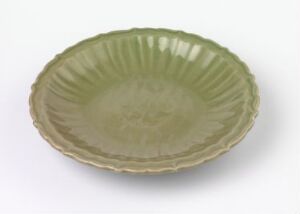  A delicate celadon green plate with a ruffled edge design on a plain, soft-focus background. The plate exhibits a semi-gloss surface that softly reflects the light.