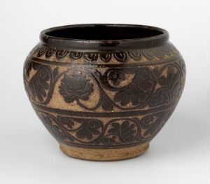  A ceramic pot with a bulbous body and narrow opening, featuring a light brown base color with black glazed rim and intricate black floral patterns etched around the middle against the beige clay.