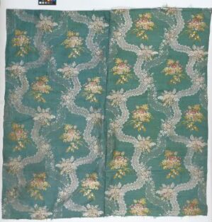  A square fabric with a repeating floral pattern, featuring a muted teal background with clusters of light yellow and peach flowers surrounded by white and soft green foliage, suggesting a vintage or traditional style.