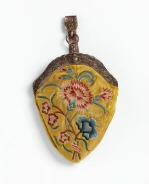  A vintage shield-shaped pendant with mustard yellow enamel and detailed floral patterns in orange, blue, and red, framed by a darker metal border, and suspended by a brown string. Artist name and title remain unknown.