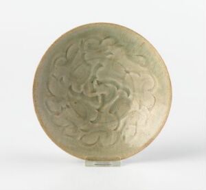  A carved, pale olive round plate or medallion with a subtle, raised swirling pattern on its surface, displayed against a plain white background.