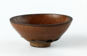  An earthenware bowl with a flared rim and a small base, displaying a gradient from dark at the rim to reddish-brown, shown against a plain white background.