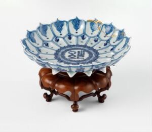  A decorative fluted porcelain bowl with blue and white design and gold trim, resting on an intricately carved wooden stand.