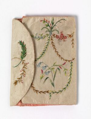  A photo of an antique embroidery on a piece of off-white fabric featuring an intertwined floral and foliage design in soft shades of green, red, blue, and yellow with frayed edges.