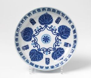  An intricately patterned round ceramic plate with a glossy finish, featuring a blue and white color scheme. The central design is a cobalt blue medallion surrounded by symmetrical circular motifs and a decorative border around the rim.