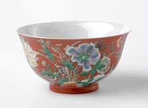  A traditional ceramic bowl with a coral pink exterior featuring an intricate pattern of blue and white flowers, green leaves, and suggestive images of birds in flight.