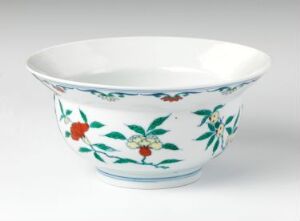  A white porcelain bowl with a tapered shape, decorated with a floral pattern of green leaves and flowers in red and blue with yellow accents, against a light-gray background. Artistname and title unknown.