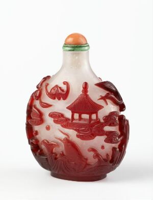  An intricately carved, traditional Chinese snuff bottle with a white and red color scheme, featuring a central pagoda-style building, surrounded by natural motifs, and a dragon design, with a small round lid at the top that has a bright accent color.