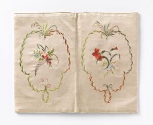  An open embrodiered fabric book with a light beige background and two pages showing. Each page has an oval garland with delicately embroidered flowers in shades of red, blue, yellow, and green. The garland borders are stitched in brownish-gold, resembling a vine or rope. The embroidery implies vintage craftsmanship, and the fabric appears aged yet well-preserved.