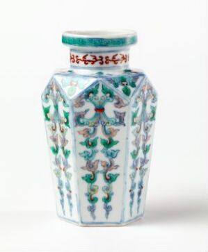  A hexagonal porcelain vase with a white background and decorative floral patterns in green, blue, and red, featuring a red band with blue and green floral designs around the neck.