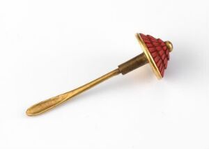  An ornate object with a red and burgundy triangular-patterned, conical top and a slender gold shaft, possibly a decorative spindle or finial, set against an off-white background.