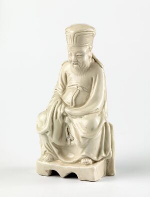  A porcelain figurine titled "Konfutse" by the Qing dynasty artist, depicting a serene and wise figure in traditional East Asian clothing, seated with hands gently resting in the lap, showcasing a creamy white glaze over subtle beige folds of the robe.