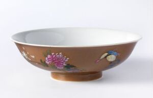  A traditional bowl with a wide opening and a rounded base, featuring a warm brown exterior with pink and white floral designs and a blue butterfly, against a plain white interior resting on a white background.