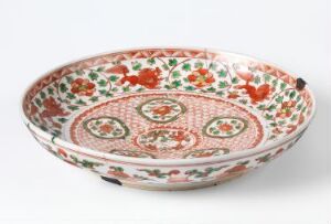  An oval-shaped shallow bowl with a detailed red and green floral and geometric pattern on a white background, suggesting an ornate and traditional decorative design.