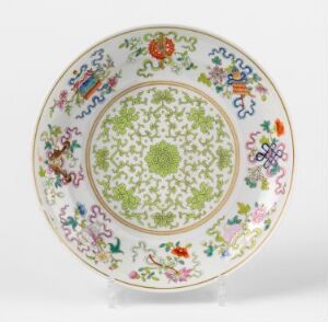  A round ceramic plate with an intricate design, featuring a lime green central medallion with lattice and floral patterns, surrounded by multi-colored floral motifs and heraldic symbols on a white background, finished with a gold-tinted rim.