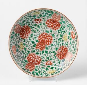  A porcelain plate with a vibrant green background featuring intricate leaf patterns and several large red and white floral designs, possibly peonies. The plate's rim is outlined in red, complementing the main design.