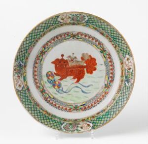  A decorative plate featuring a central stylized red-orange animal on a pale background with blue waves beneath it, surrounded by small greenery motifs, and an intricate outer rim with a geometric pattern in greens, reds, and blues. Artist name and title are unknown.