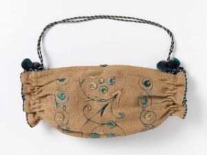  Antique oblong purse made of light beige or tan soft fabric with intricate teal and dark blue embroidery of vines and flowers, featuring a twisted metal handle and plush dark tassels, against a plain, light background.