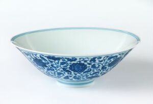  A porcelain bowl with elaborate blue floral patterns on its exterior against a neutral off-white background. The inside of the bowl is a smooth glossy white.