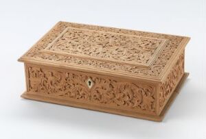  An intricately carved light brown wooden box with floral and foliage motifs, featuring a hinged lid and a keyhole on the front, displayed against a plain, neutral background.