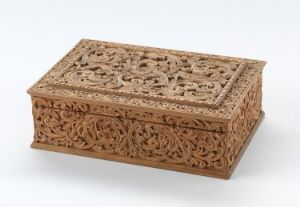  A rectangular, intricately carved wooden box with ornate floral patterns on a light grey background, displaying a warm, light brown color and fine craftsmanship.