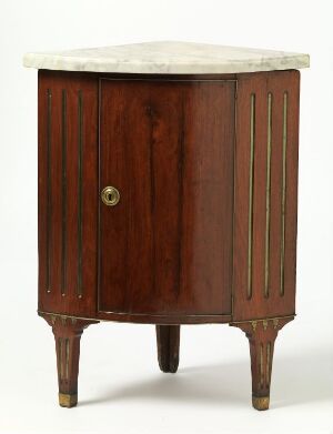  A classical-style corner cabinet with a curved front, featuring rich reddish-brown mahogany wood with vertical inset panels, standing on tapered legs with light-colored caps, a central door with a brass knob, and a white marble top with subtle veining.