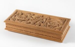  An intricately carved wooden box with floral designs and geometric patterns, exhibiting a warm mid-brown color with visible wood grain.