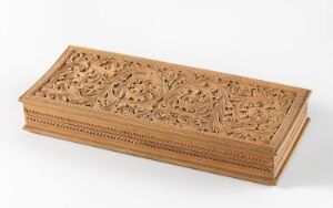  An ornate, rectangular wooden box with elaborate floral and foliage carvings on the top and geometric patterns along the sides, displayed on a plain background.