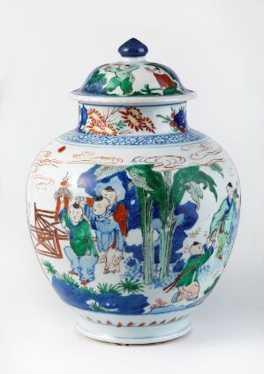  A traditional white ceramic jar with a lid, featuring colorful hand-painted scenes with human figures in green, blue, and red traditional attire, set against a backdrop of green foliage and architectural elements, topped with a cobalt blue lid with a round handle.