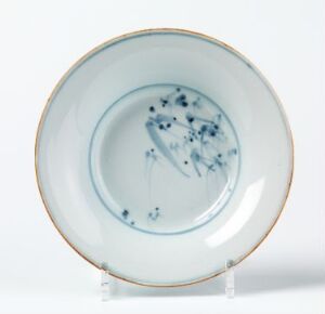  A white porcelain plate with a delicate design featuring sparse blue floral patterns in the center and a thin gold rim, presented on a clear plate stand against a neutral background.