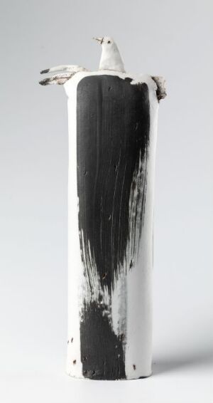  A tall, slender ceramic vase with a white base color and a dramatic, vertical stroke of black glaze descending from the rim. Two elongated bird-like figures emerge from the top, one arching over the rim with its head pointed upwards, adding an organic element to the modern piece.