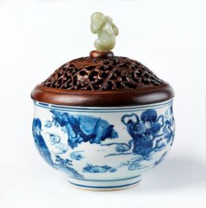  A porcelain container with a blue and white pattern featuring traditional Chinese landscapes, topped with a brown lattice-work lid and a green jade grape finial.